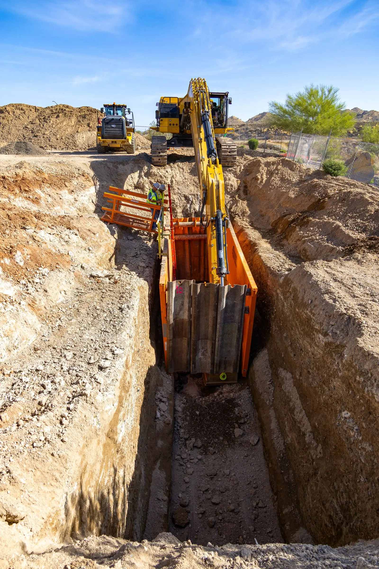 Aerial view looking down a long utility trench with an excavator at the far end